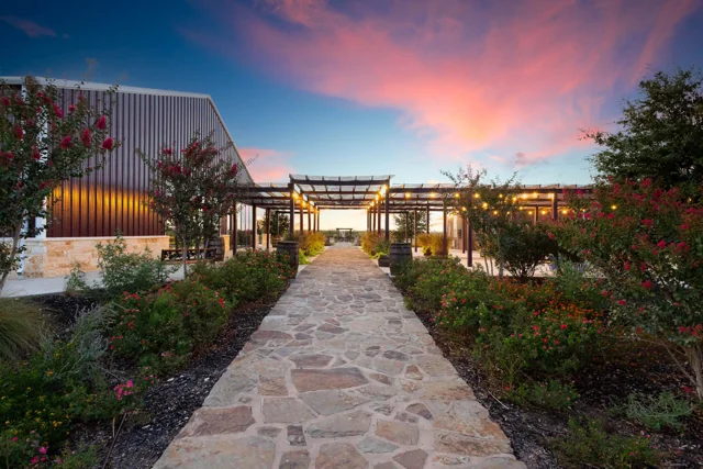A garden path leads toward the illuminated courtyard at sunset