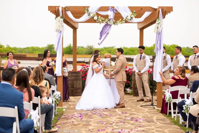A couple exchanges vows beneath a flower-decorated outdoor pergola