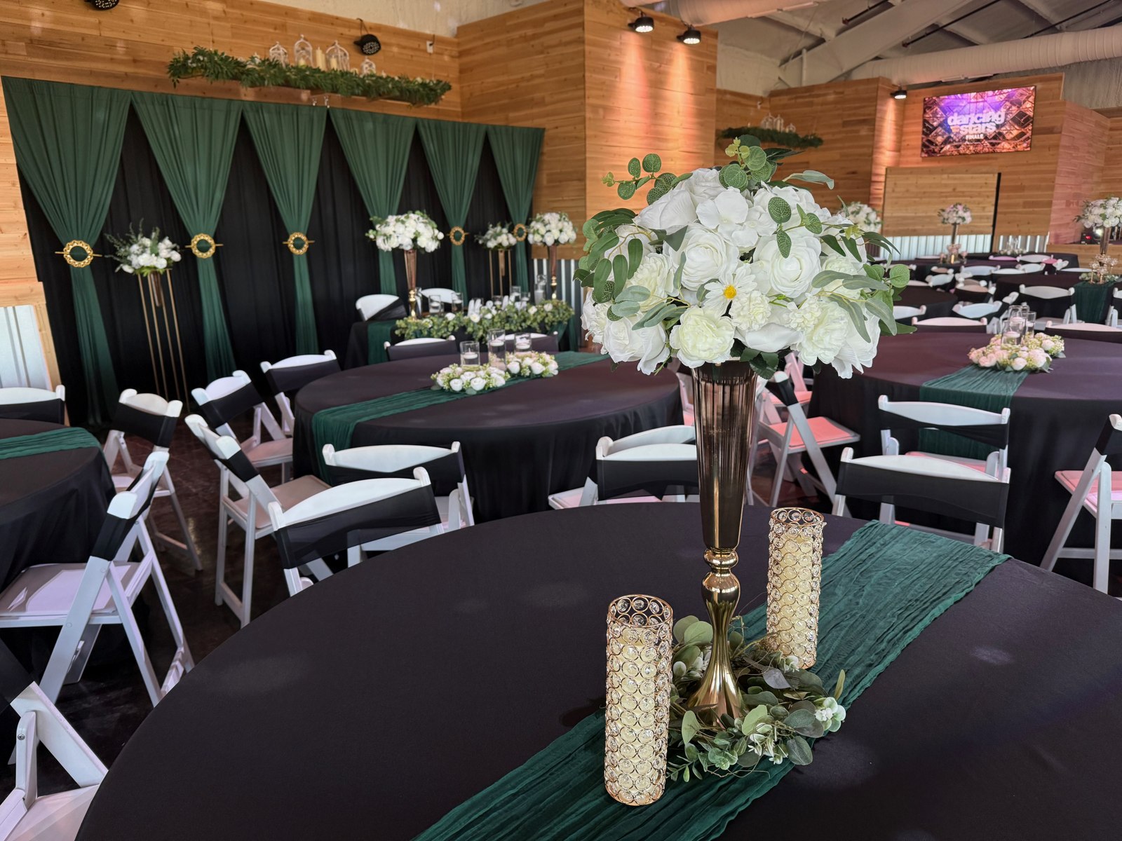Tall white floral centerpieces above emerald and gold table settings