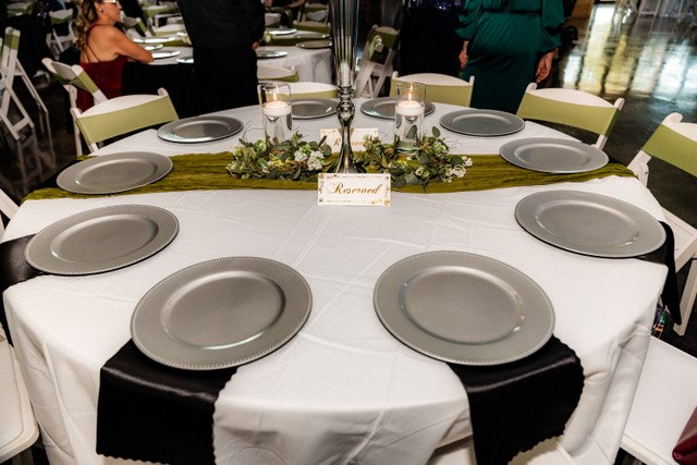 Round reception table with greenery, white linens and silver charger plates