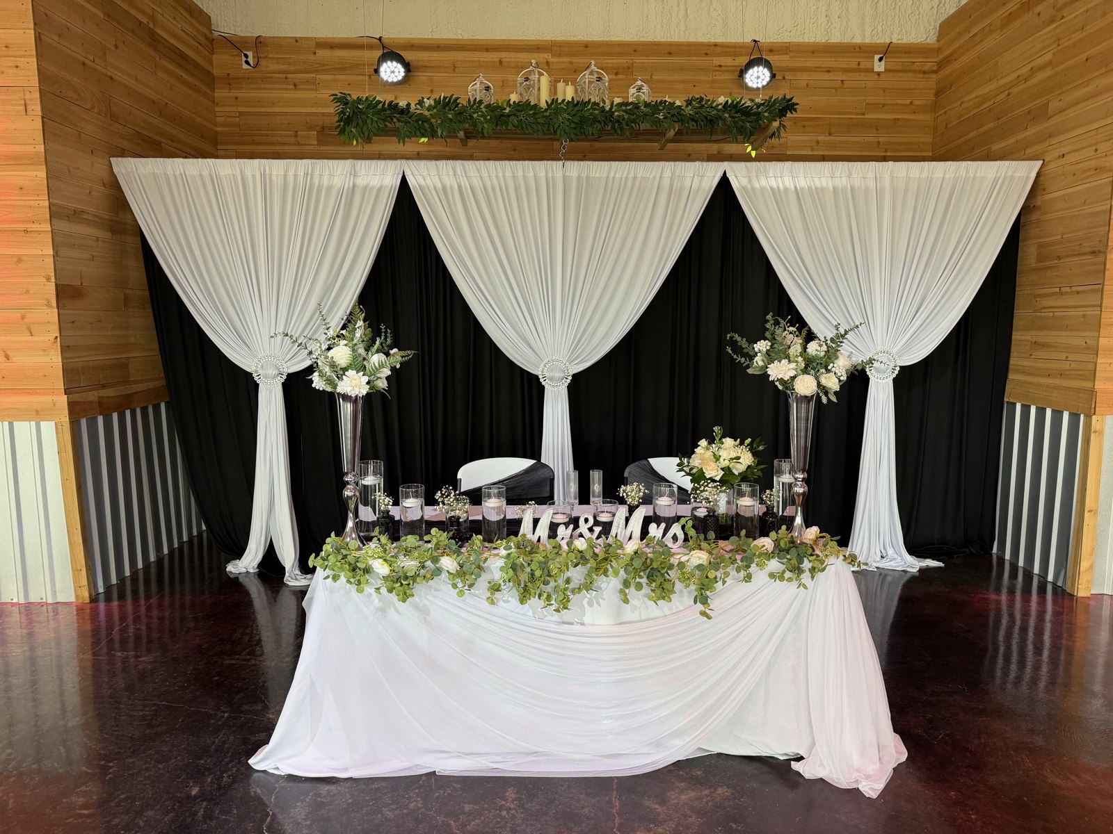 White sweetheart table with floral greenery and draped backdrop