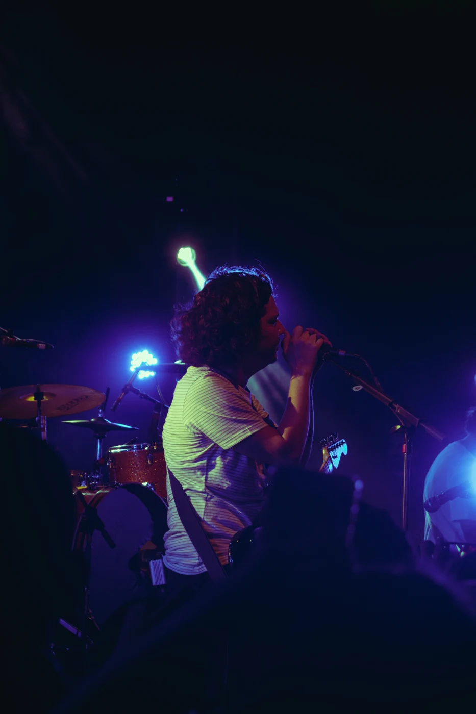 A singer performing with a guitar under blue and purple stage lights