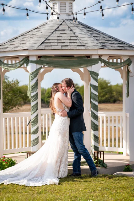 A couple shares a kiss beneath the white gazebo