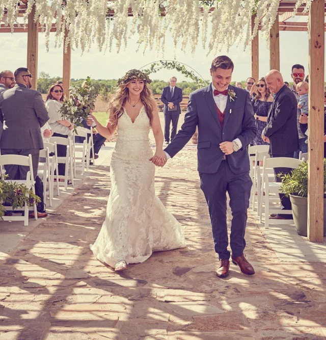 A newlywed couple walks through the pergola with their wedding party