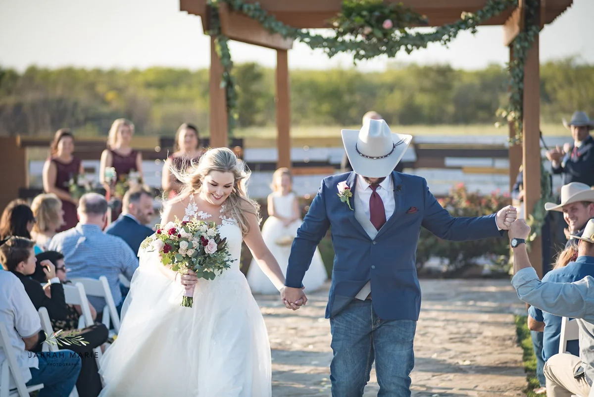 A newlywed couple celebrates with guests while walking down the outdoor aisle