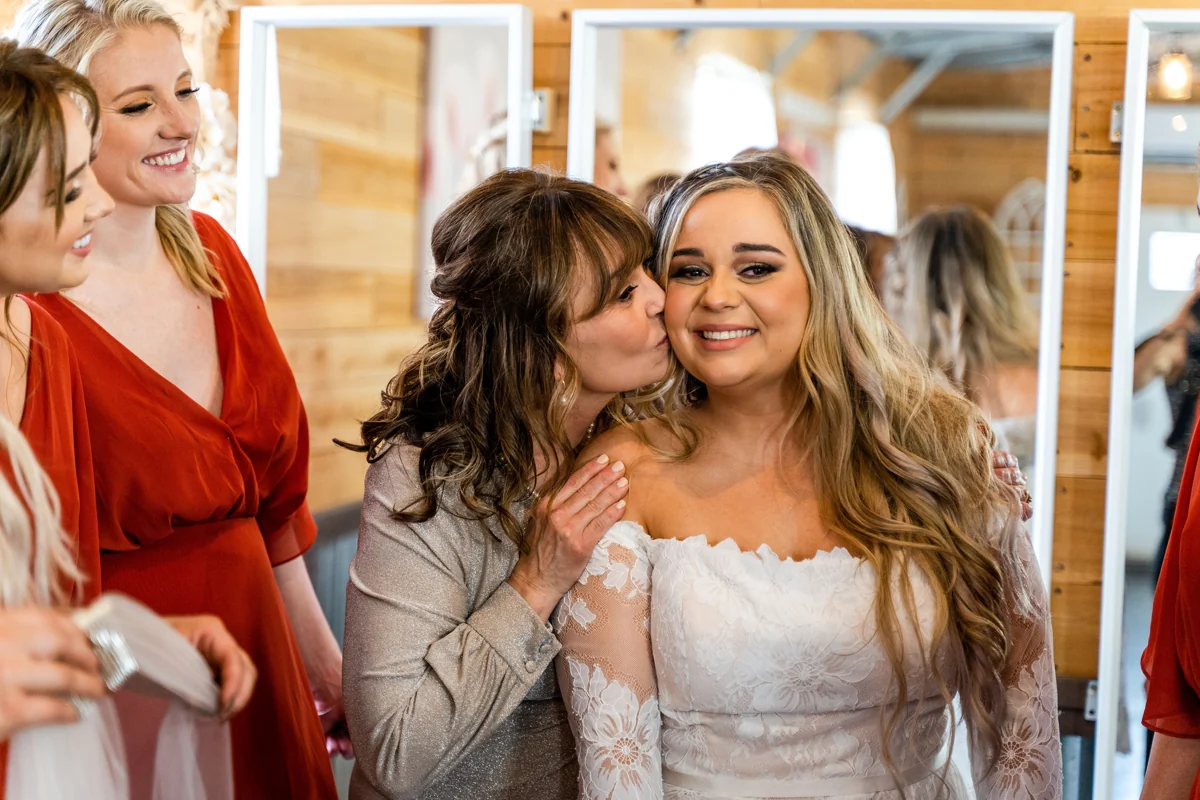 A smiling bride receives a kiss on the cheek from a loved one