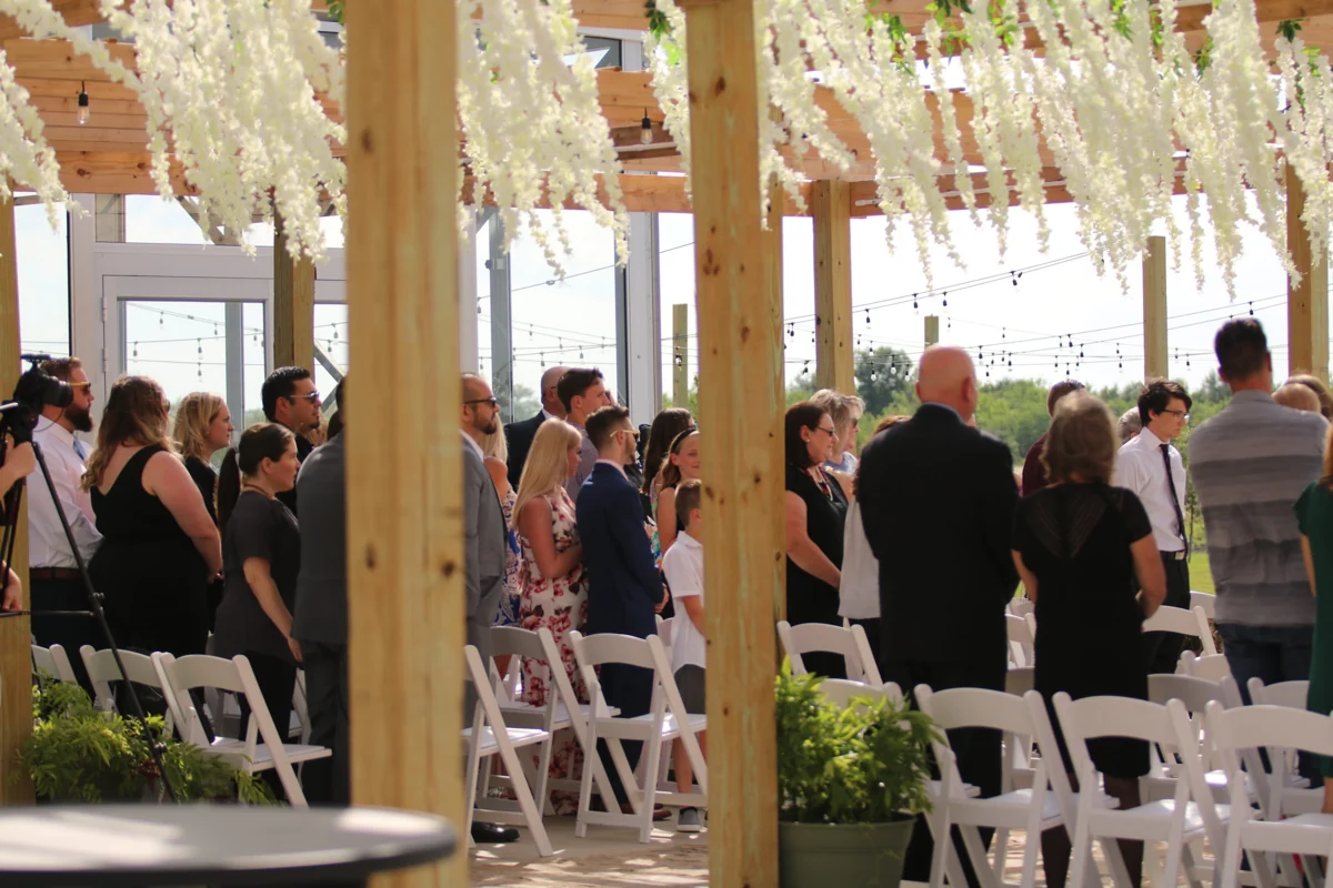 Friends and family gather beneath white flowers in the sunlit pergola